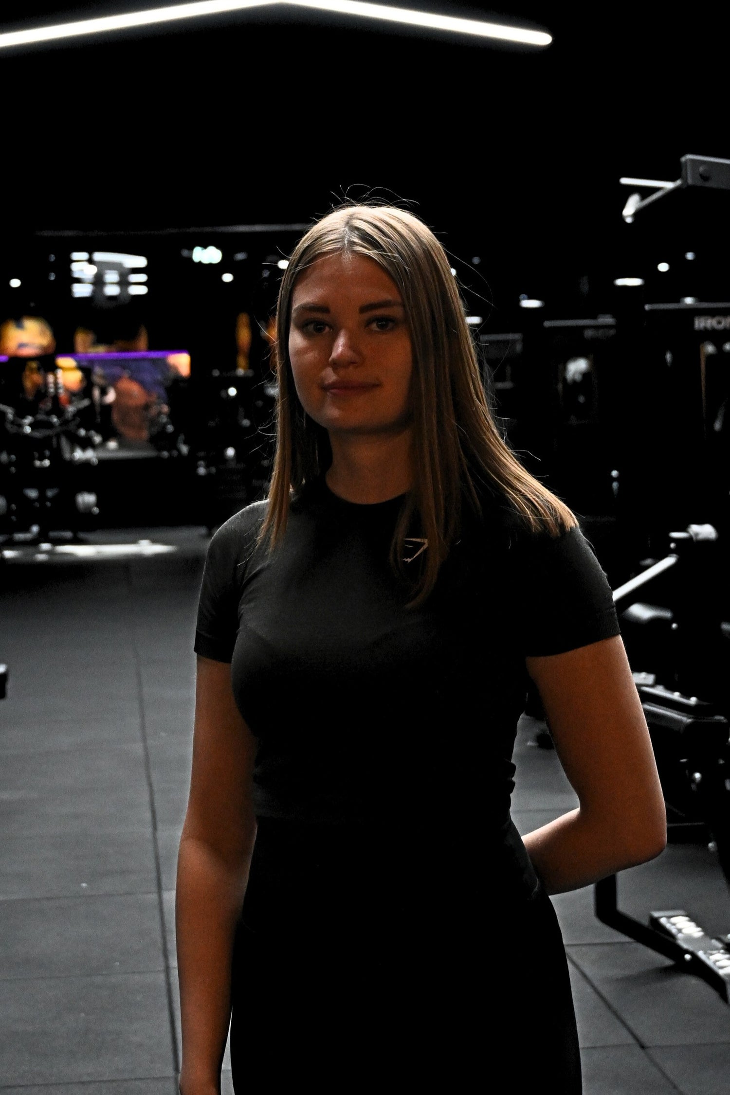 Naispuolinen personal trainer poseeraa kuntosalilla treeniympäristössä.