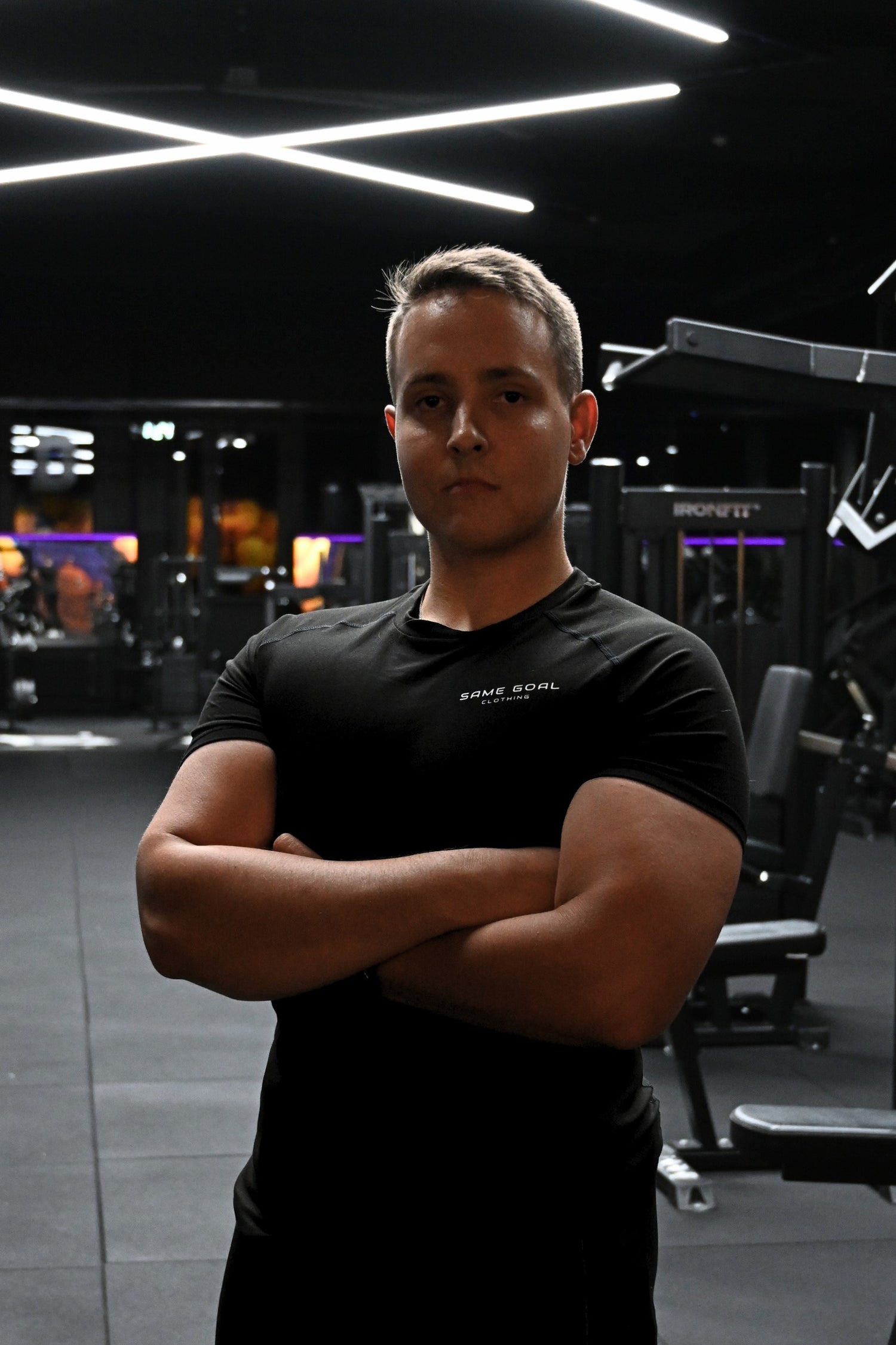 Personal trainer poseeraa kuntosalilla kädet ristissä treeniympäristössä.